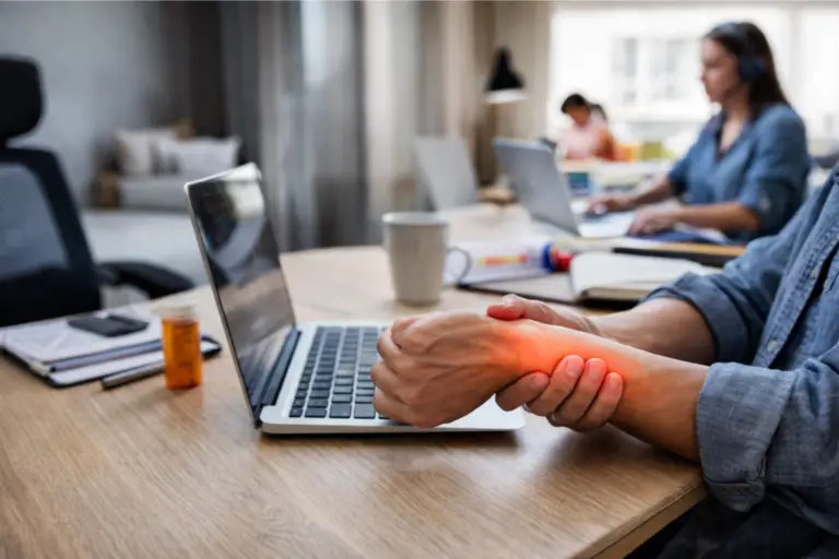 Person holding their wrist while working on their laptop